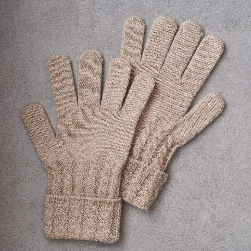 A pair of beige cable-knit gloves laid flat on a textured gray background.