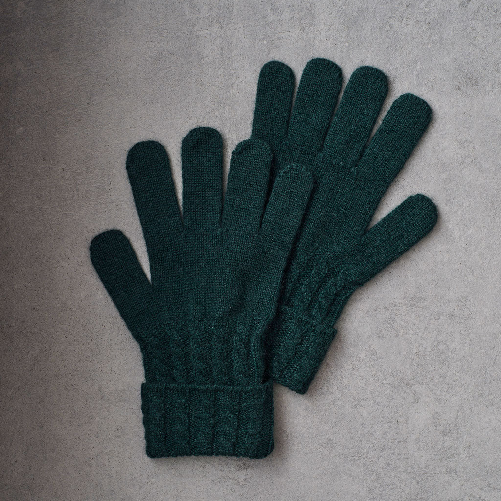 A pair of dark forest green knit gloves laid flat on a textured gray surface.