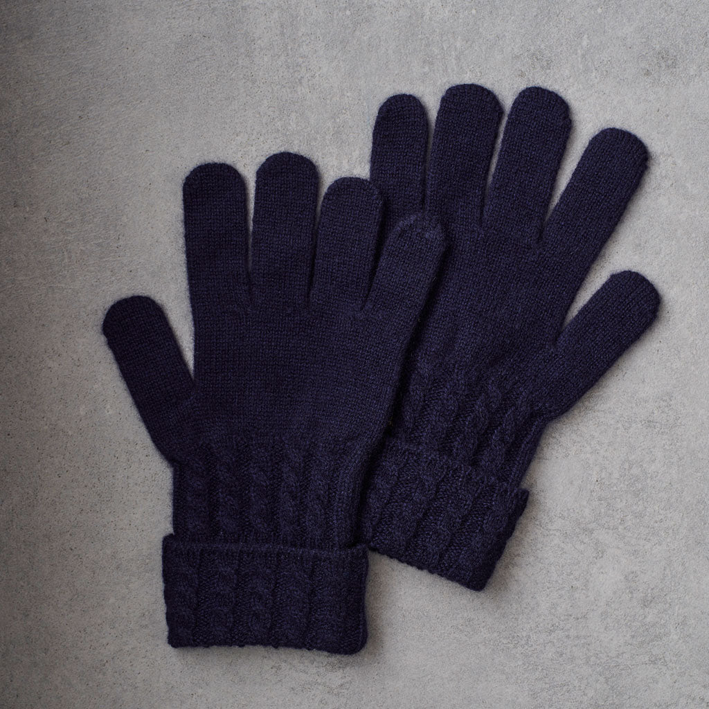 A pair of dark navy blue cable-knit gloves laid flat on a textured gray surface.