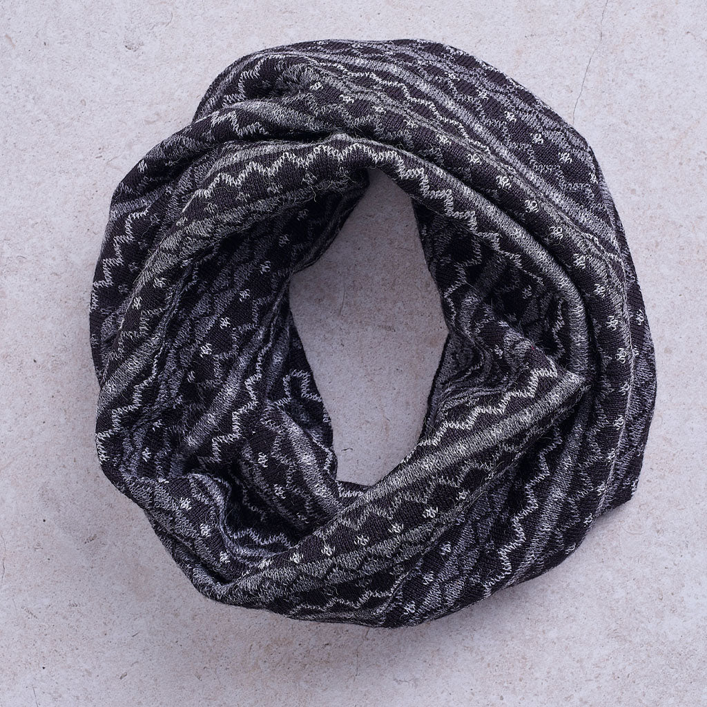 a dark charcoal gray infinity scarf with a white geometric pattern, against a solid grey background.