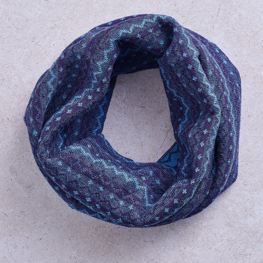 A blue infinity scarf with a white geometric pattern, against a solid grey background.