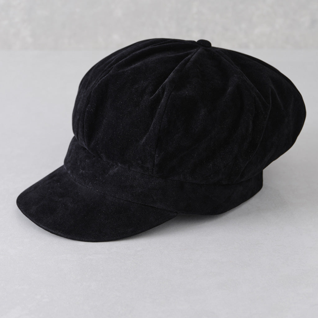 A black velvet newsboy cap with a curved brim, photographed on a light gray textured background.