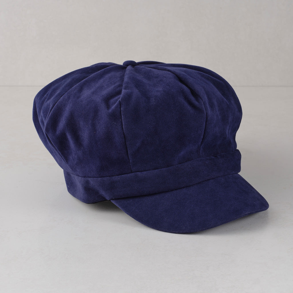 A dark navy blue velvet newsboy cap with a curved brim, photographed on a neutral light gray background.