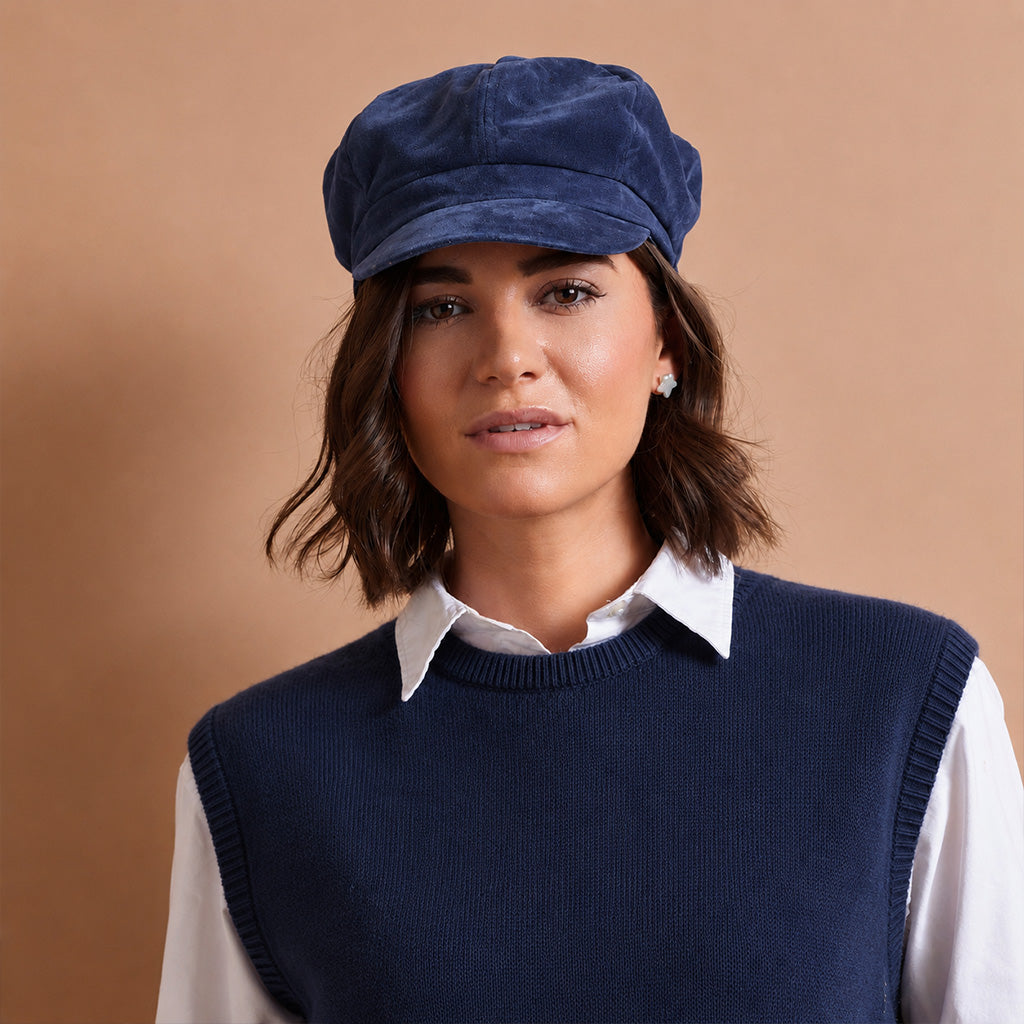 a women wearing a dark navy blue velvet newsboy cap with a curved brim, photographed on a neutral light gray background.