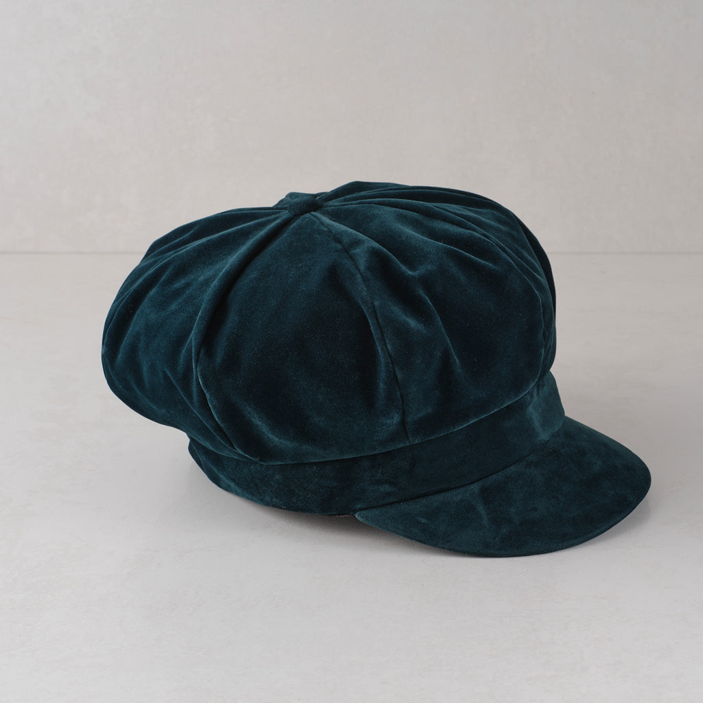 A dark teal green velvet newsboy cap with a rounded crown and a short flat brim, shown on a light gray background.