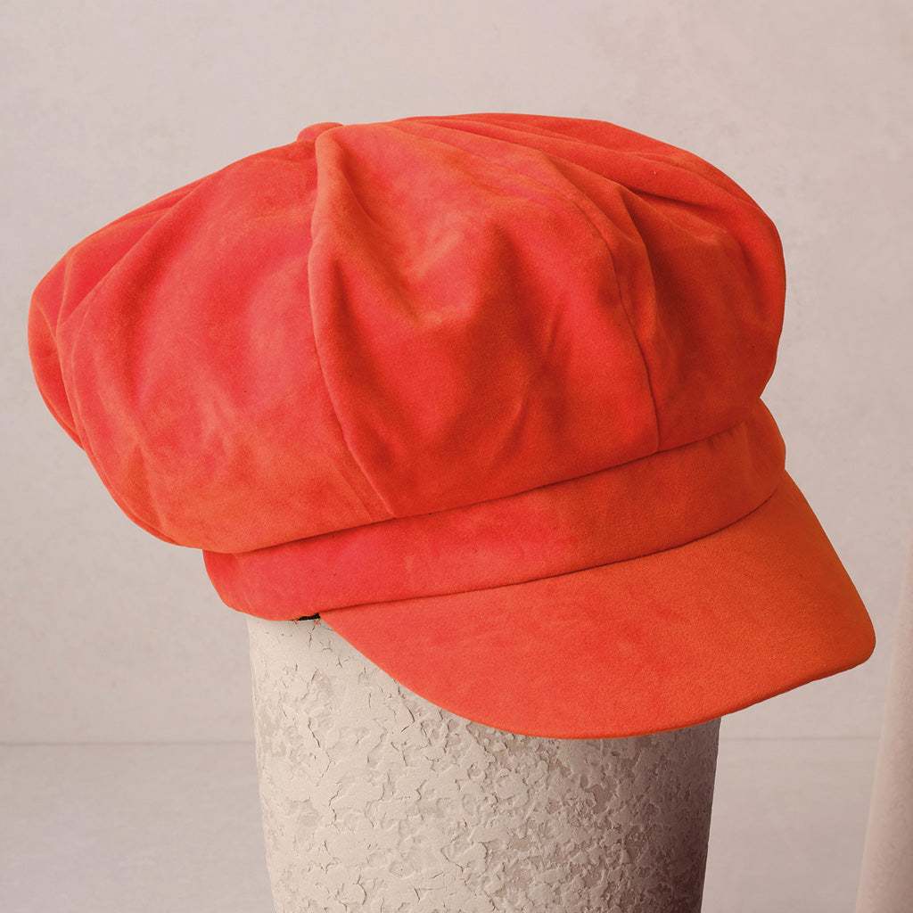 An orange baker boy cap on grey background.