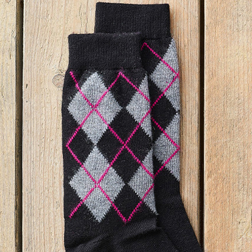 A pair of black crew socks with a gray and black argyle pattern outlined in bright pink, laid flat on a light wood plank background.