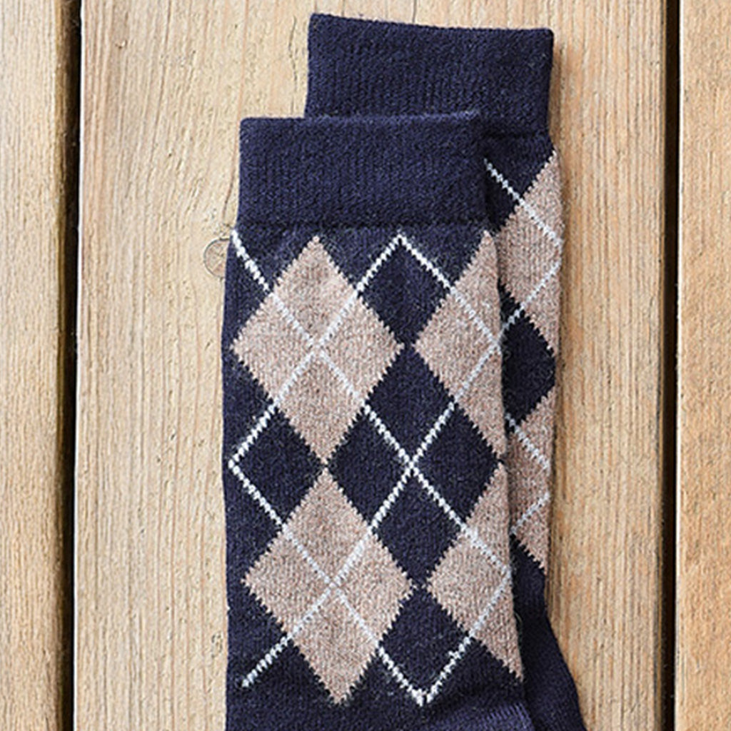 A pair of navy blue socks with a beige and white argyle pattern, folded on a light brown wooden plank background.