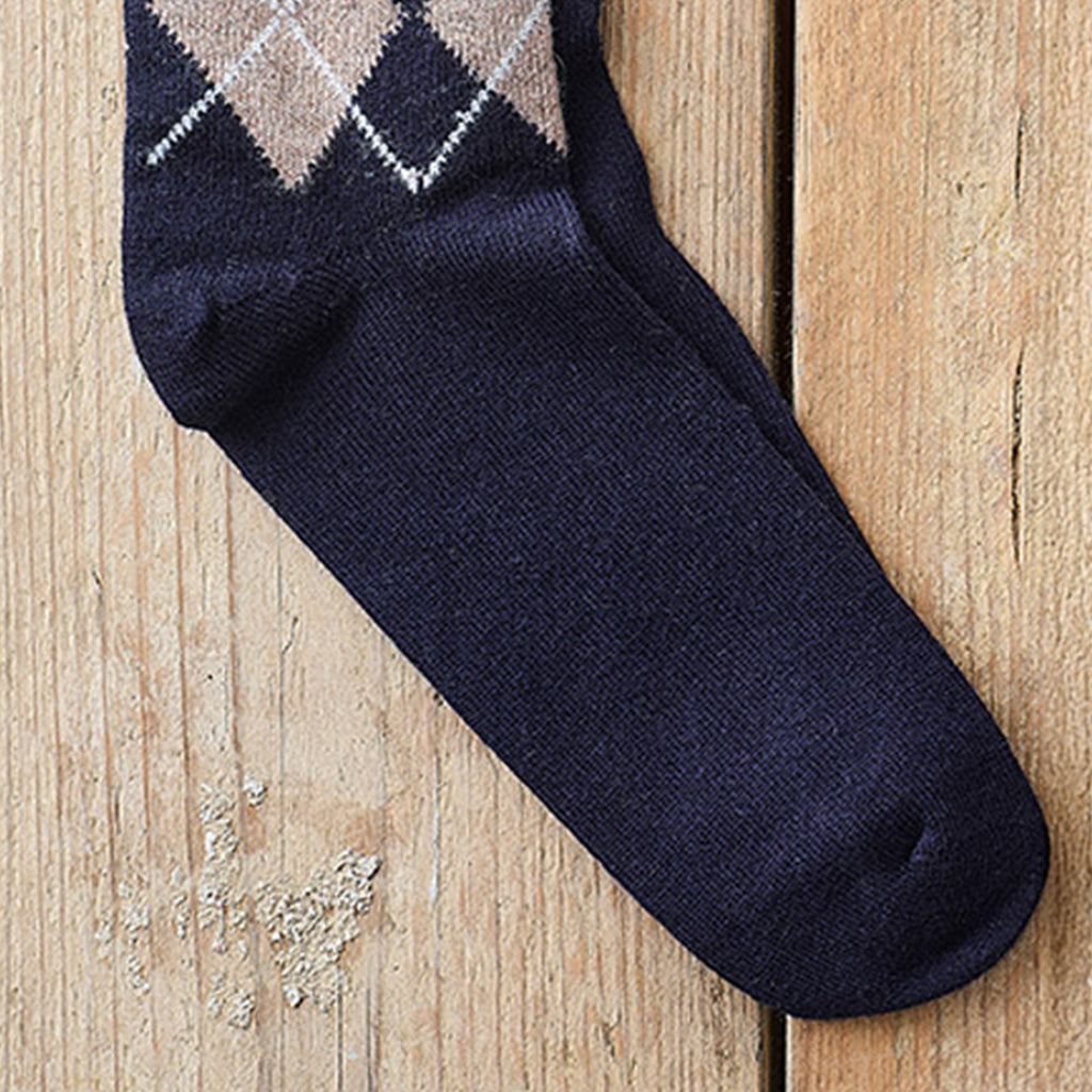 A single navy blue crew sock with an argyle pattern in beige, brown, and white near the cuff, laid diagonally on a light wood plank surface.