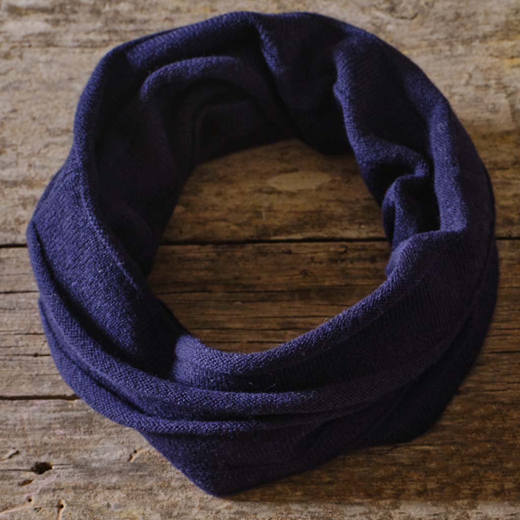 A dark navy blue infinity scarf made of soft knit fabric, arranged in a loop on a rustic wooden surface.