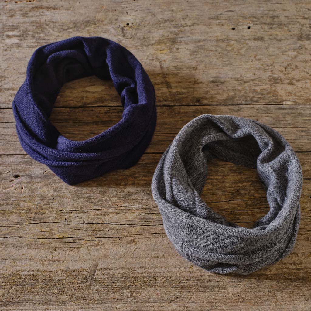 Two fabric neck warmers, one in dark navy blue and the other in heather gray, displayed on a rustic wooden surface.