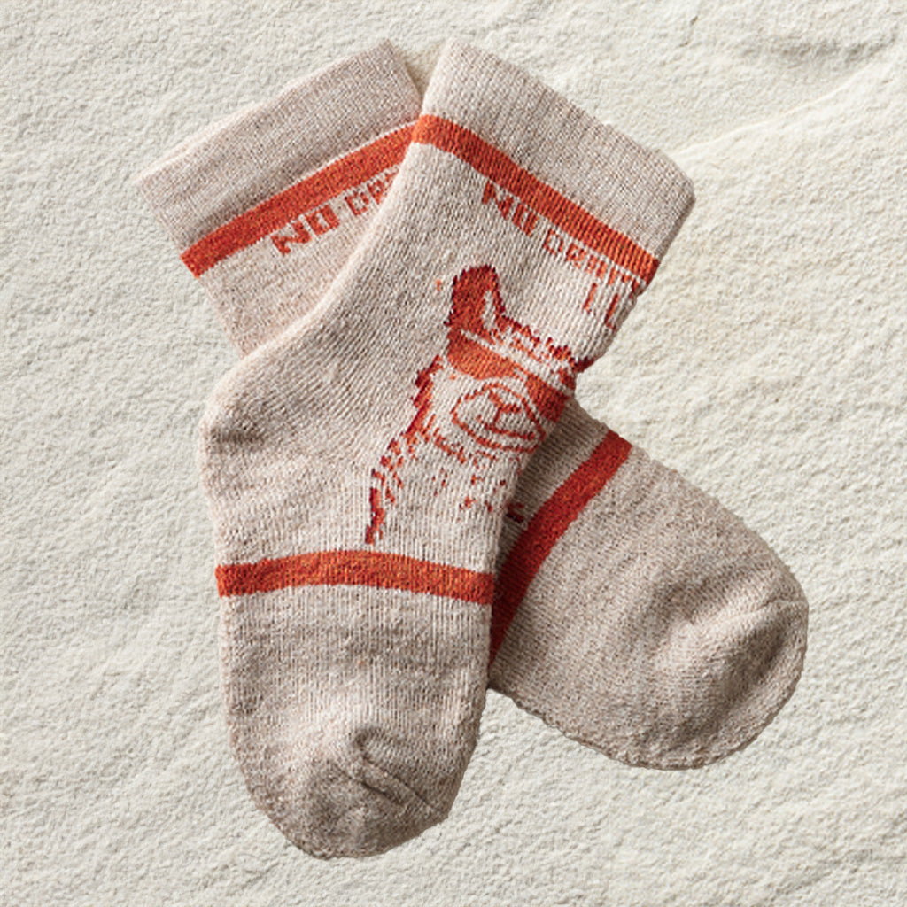 A pair of beige crew socks with orange-red stripes and a distressed orange-red graphic, laid flat on a textured off-white surface.