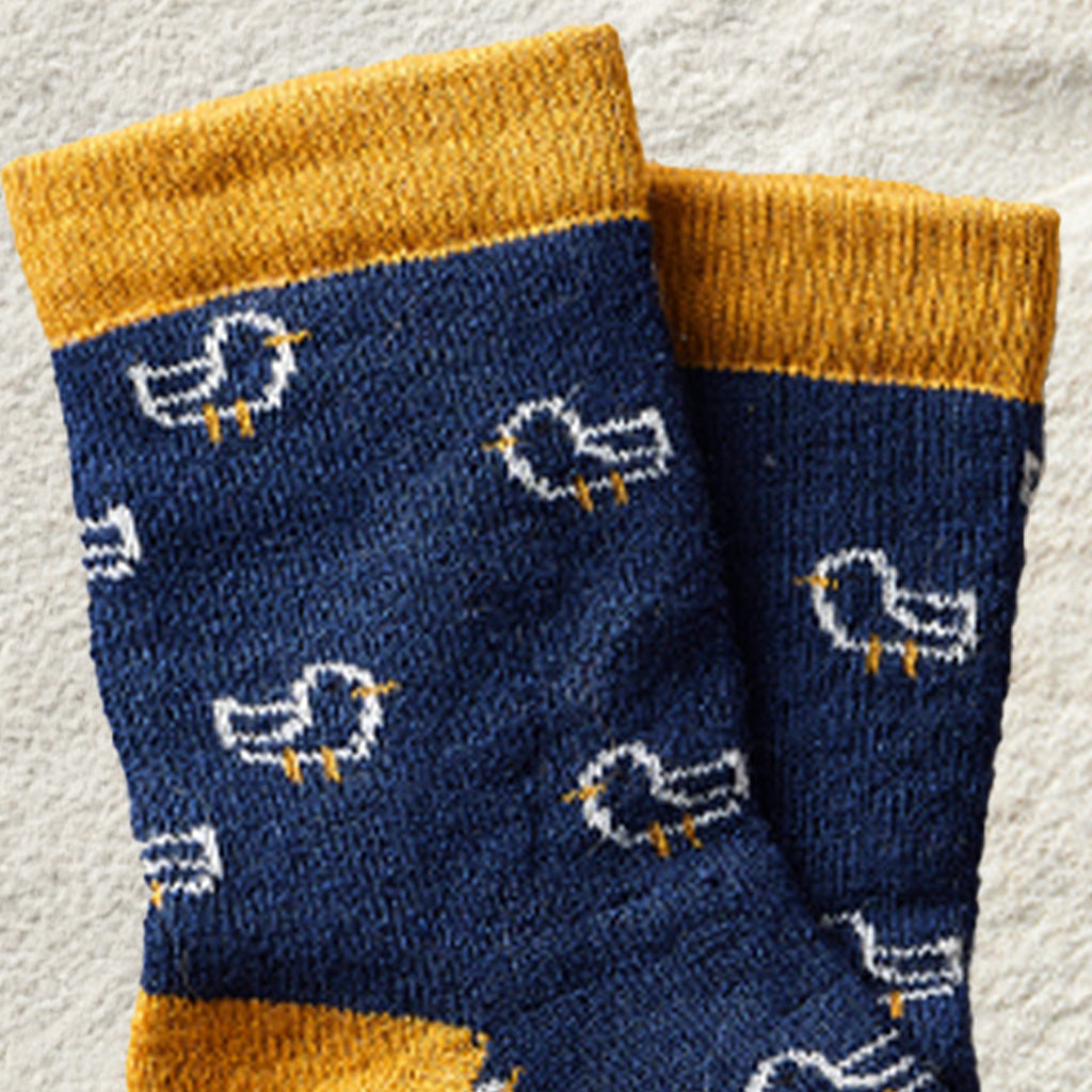 A pair of navy blue knit socks with mustard yellow cuffs and heels, featuring a white and yellow bird pattern, displayed on a textured light gray background.