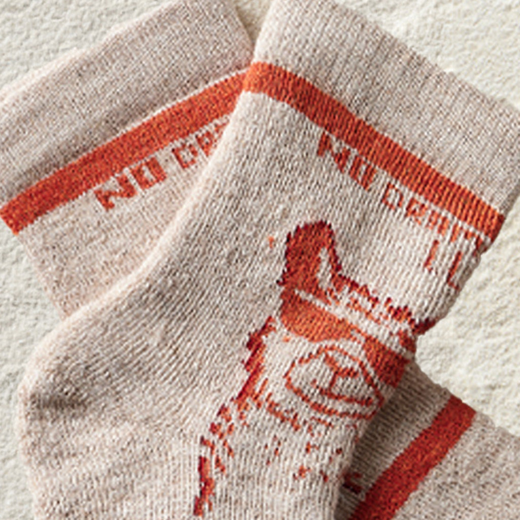 A close-up of a pair of beige knit socks with rust-orange stripes and a distressed orange graphic print, laid flat on a textured off-white background.
