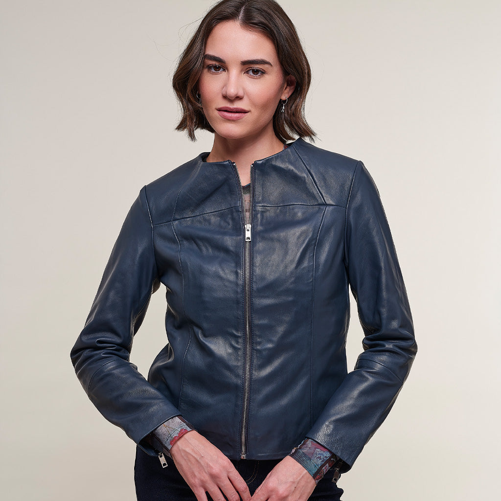 A woman wearing a dark navy blue leather jacket with a front zipper, photographed against a plain light beige studio background.