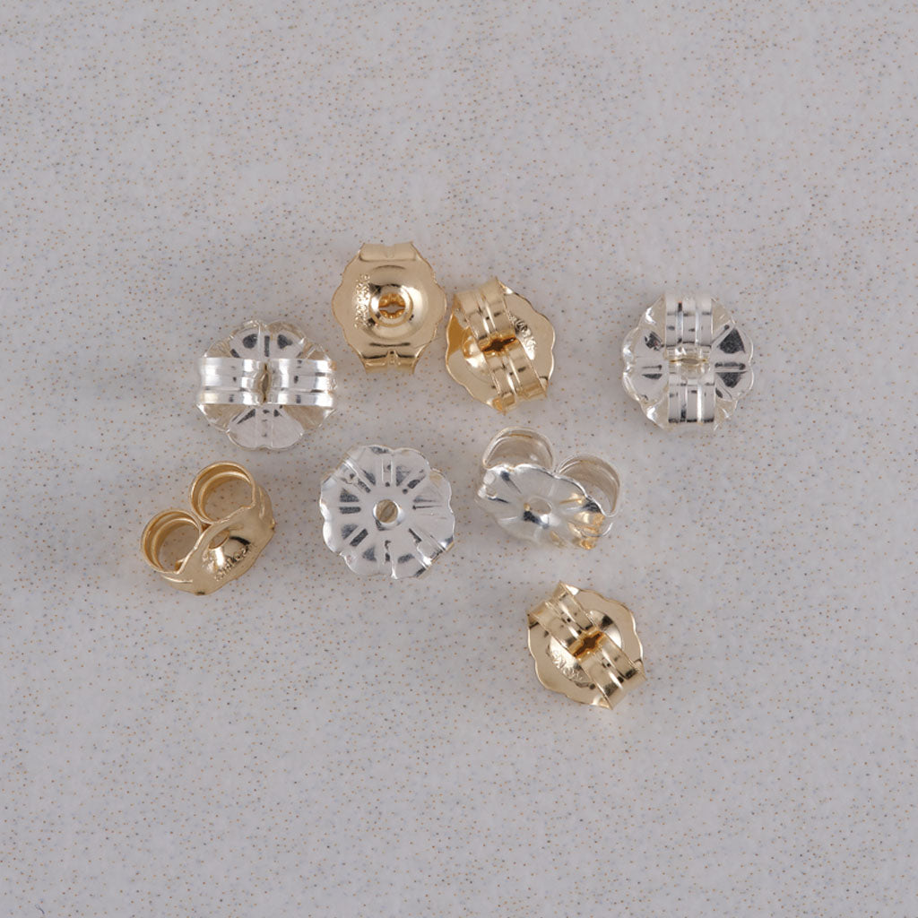 Nine small flower-shaped metal findings in gold and silver finishes arranged on a light gray textured surface.