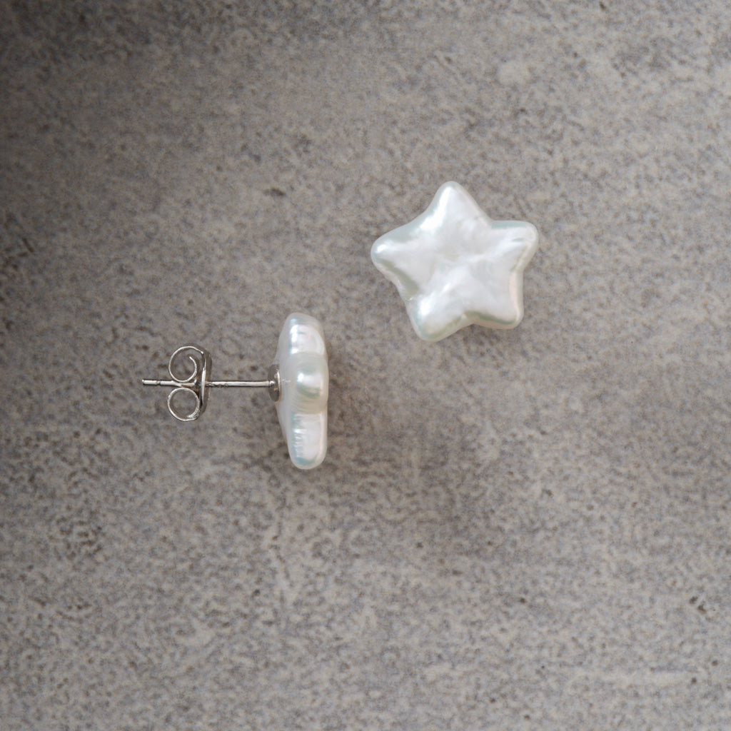 A pair of pearl stud earrings on a textured gray background, featuring one star-shaped pearl and one baroque-shaped pearl with a silver post.