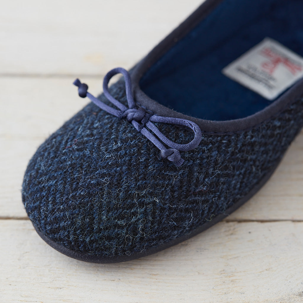 A close-up of a dark navy blue knit slipper with a matching fabric bow on the toe, resting on a light-colored wooden surface.