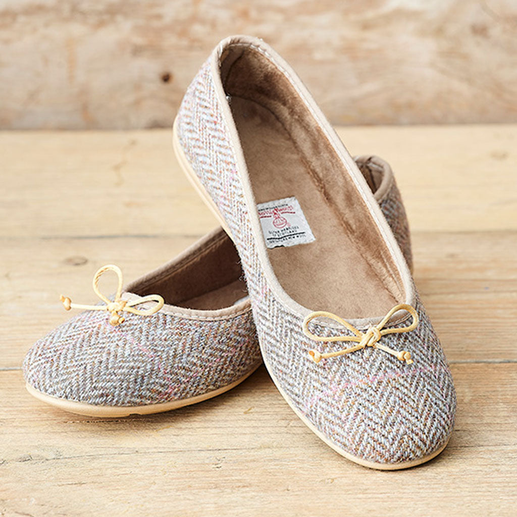 A pair of women's flat shoes with a gray and beige herringbone tweed upper, featuring a small beige ribbon bow on the toe with a tiny gold bead accent, photographed on a rustic wooden surface.