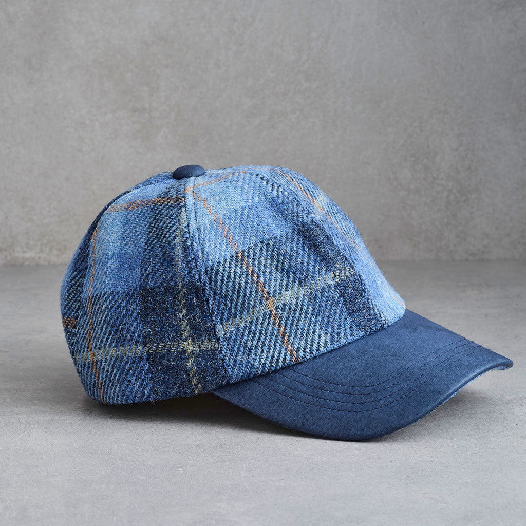 A blue plaid baseball cap with a solid blue curved brim, photographed on a textured gray background.