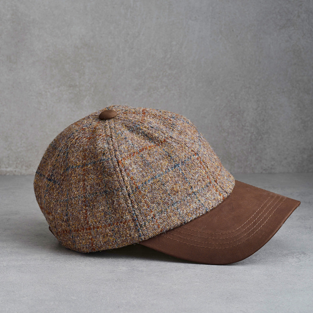 A classic six-panel tweed baseball cap with a brown leather visor and button, shown from a side profile on a gray textured background.