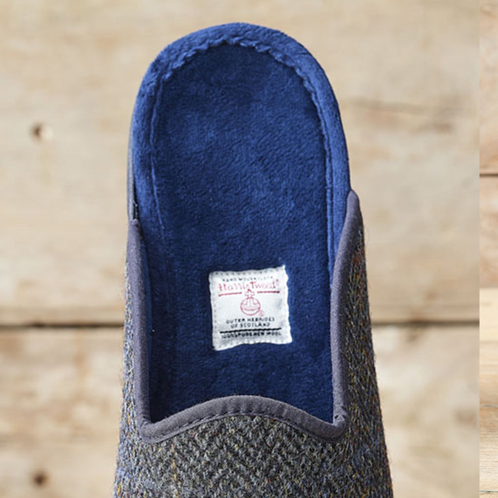 A single slip-on mule shoe shown from the top, featuring a blue herringbone tweed upper and a deep blue plush interior. A white vintage-style brand label reading 'Majestic' is visible inside the opening, set against a light wood plank background.