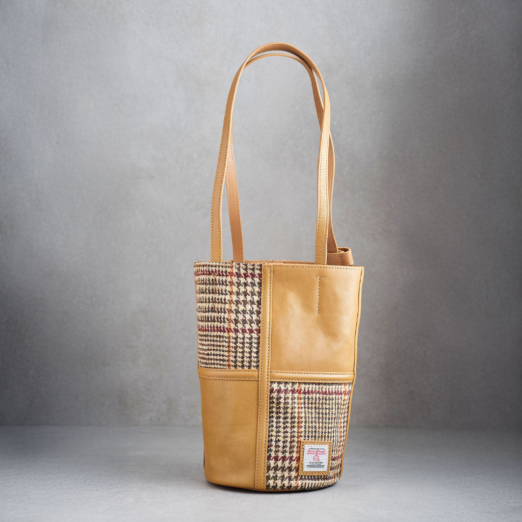 A tan leather bucket bag with a houndstooth patterned panel on the front, featuring a single shoulder strap and the ISLANDER logo embossed on the lower right front.