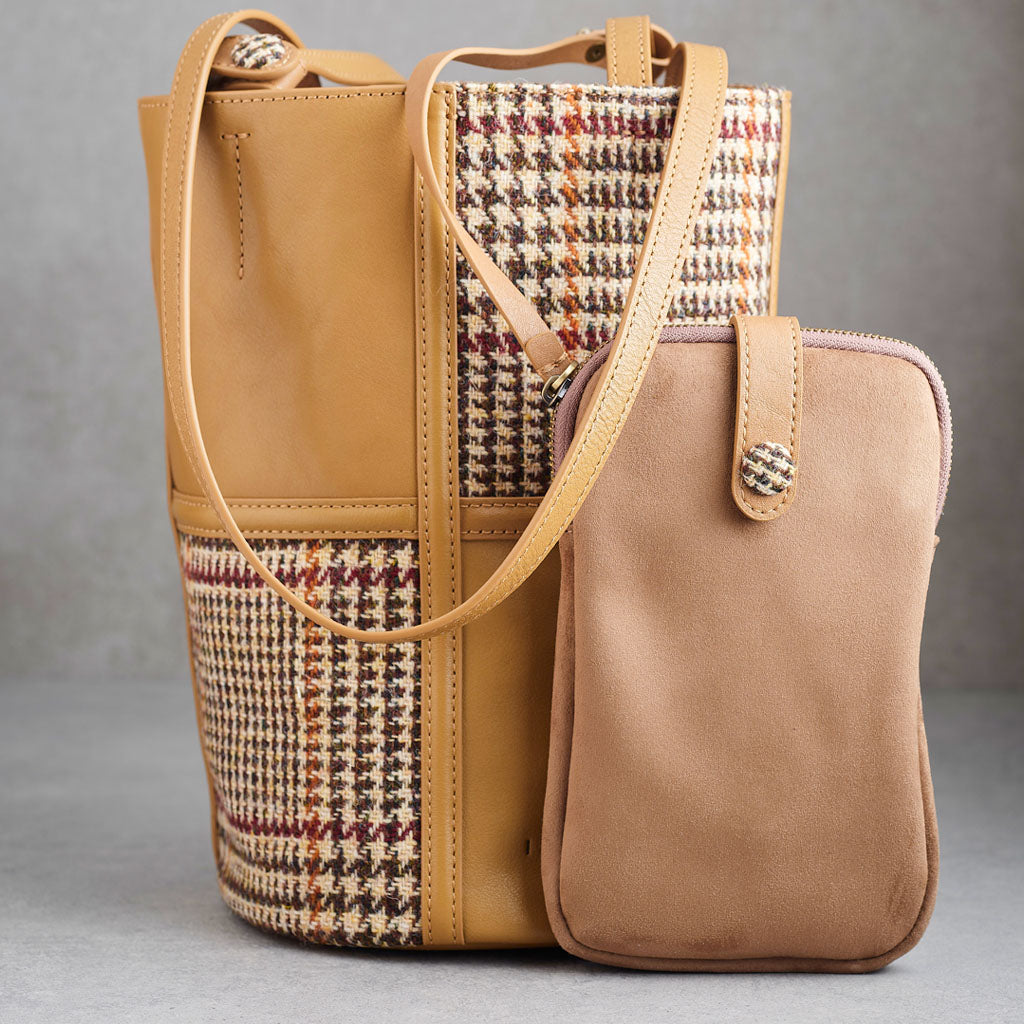 A tan leather bucket bag with a houndstooth patterned panel on the front, featuring a single shoulder strap and the ISLANDER logo embossed on the lower right front.