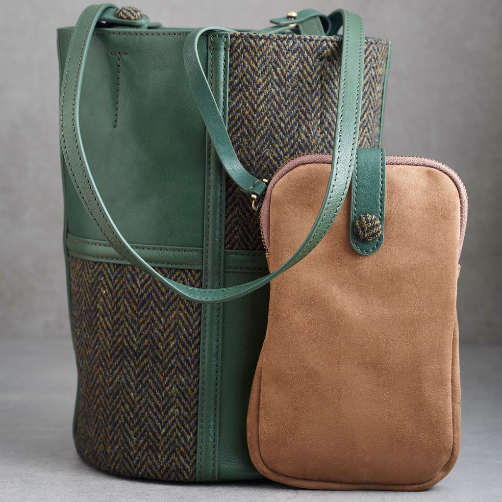 A green leather and herringbone tweed bucket bag with dual shoulder straps and a visible Woolworths label patch on the lower front, photographed against a neutral gray background.