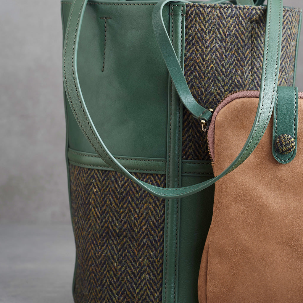 A green leather and herringbone tweed bucket bag with dual shoulder straps and a visible Woolworths label patch on the lower front, photographed against a neutral gray background.
