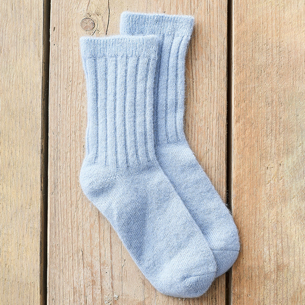 A pair of light blue ribbed crew socks laid flat on a light brown wooden plank surface.