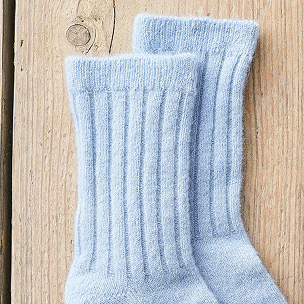 A pair of light blue ribbed knit crew socks laid flat on a light wood surface.