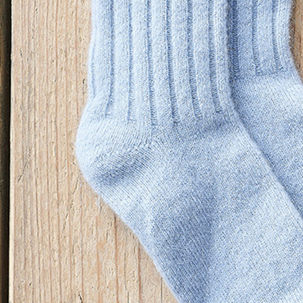 A close-up of a light blue ribbed knit sock laid on a light wood surface.
