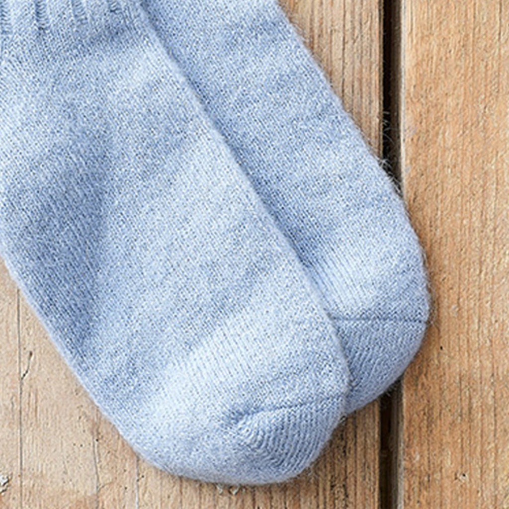 A close-up of a pair of light blue heathered knit socks resting on a rustic wooden surface.