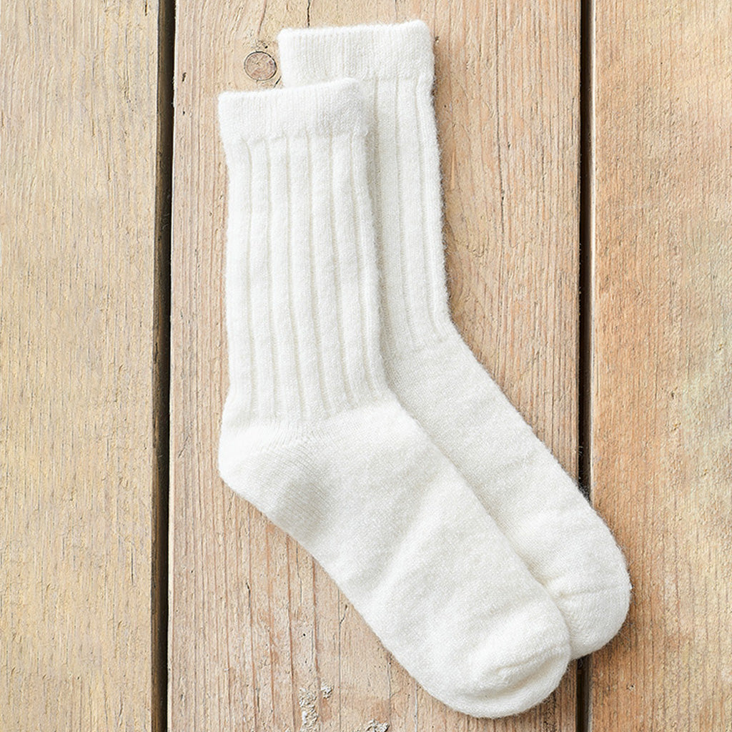 A pair of off-white ribbed crew socks laid flat on a light brown wooden plank surface.