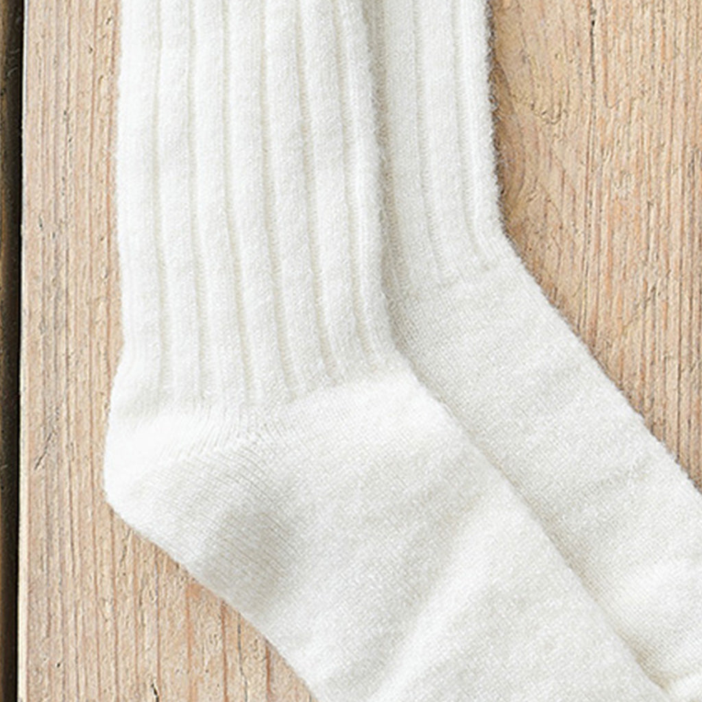 A pair of off-white ribbed knit socks laid flat on a light wood surface.