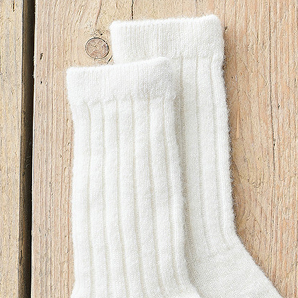 A pair of white ribbed knit socks displayed on a light-colored wooden surface.