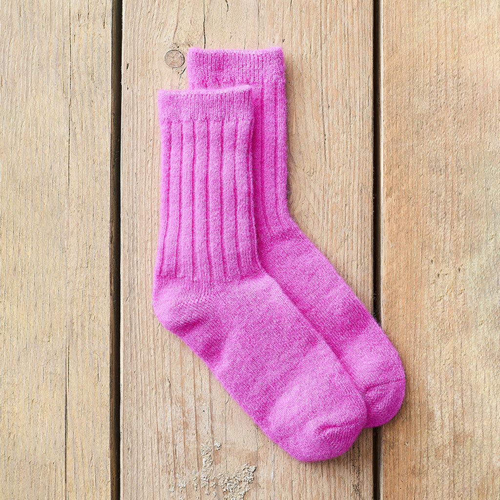 A pair of bright pink ribbed crew socks laid flat on a light wood plank surface.
