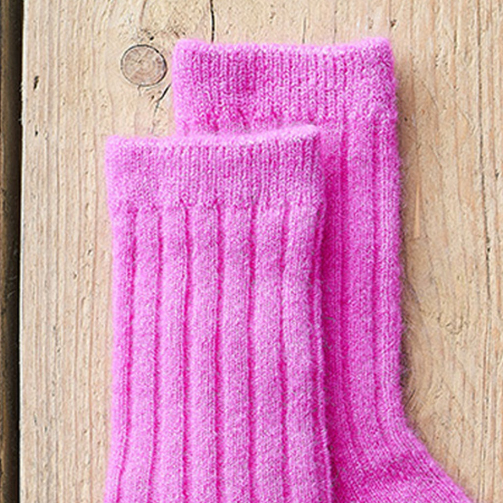 A pair of bright pink ribbed knit socks displayed on a light-colored wooden surface.