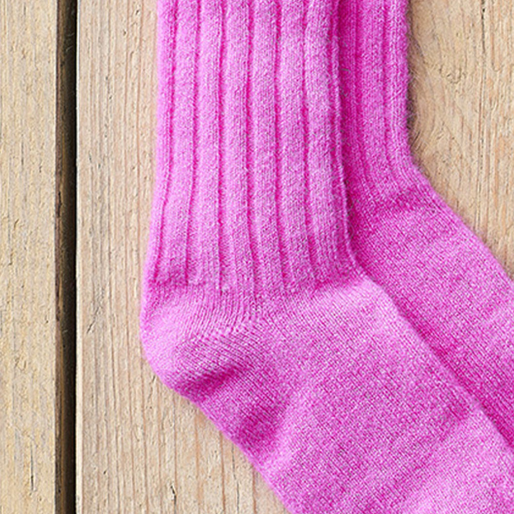 A close-up of a bright pink ribbed knit sock laid on a light wood plank surface.
