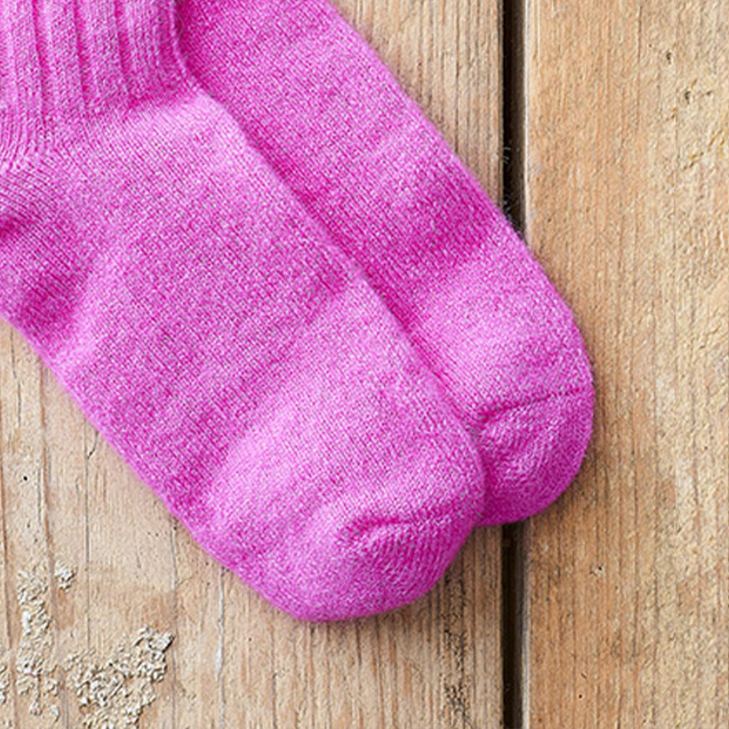 A pair of bright pink knit socks laid flat on a light brown wooden surface.