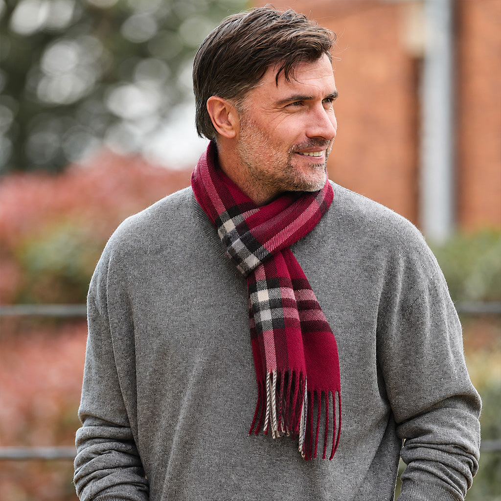 A man wearing a gray knit sweater and a burgundy plaid scarf with black and white stripes, photographed outdoors with a blurred background.