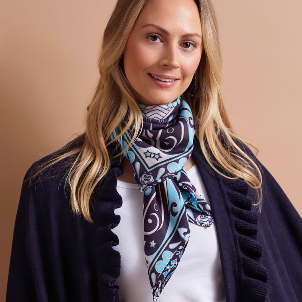 A woman wearing a navy blue and turquoise paisley scarf with white accents, styled around her neck over a white top and a dark navy cardigan.