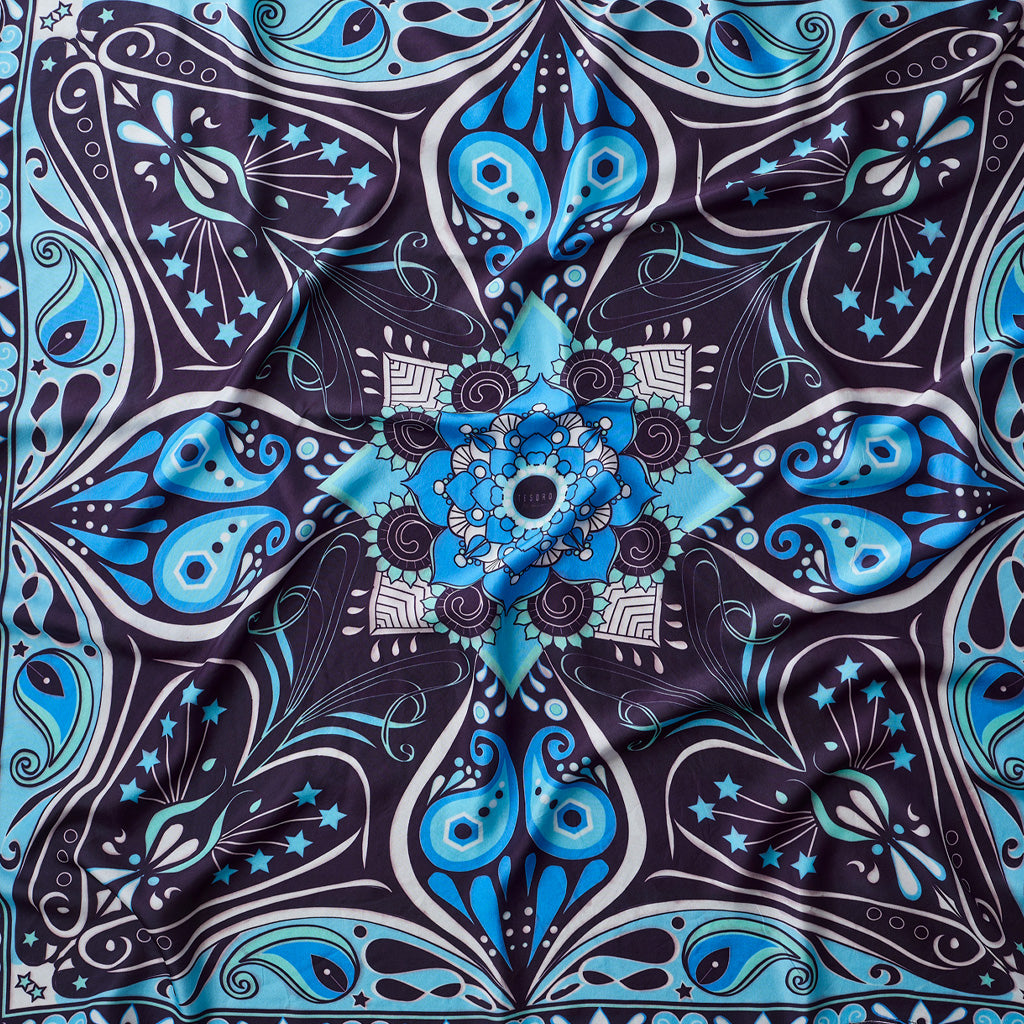 A square scarf with a symmetrical mandala pattern in shades of blue, black, and white, featuring paisley and star details.