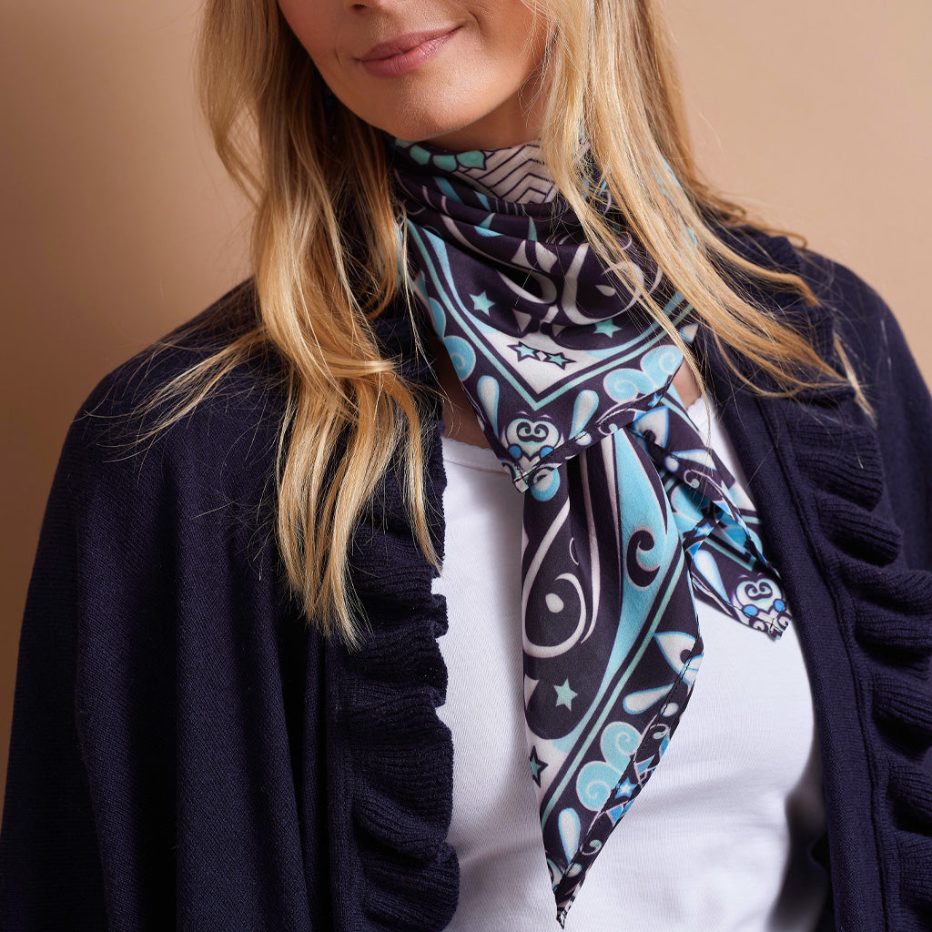 A close-up of a woman wearing a navy blue cardigan over a white top, with a patterned scarf wrapped around her neck. The scarf features a black, white, and light blue paisley design.