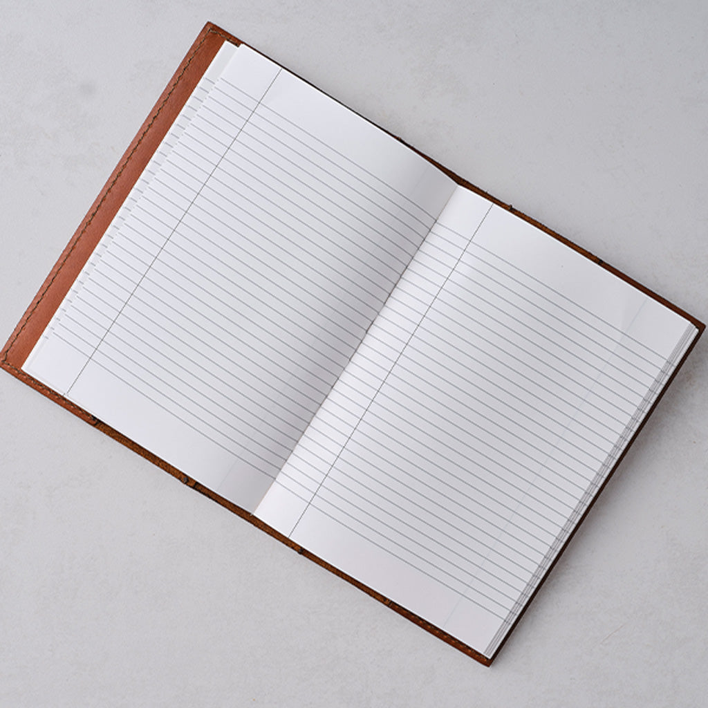 An open lined notebook with white pages and a brown cover, photographed from above on a light gray surface.