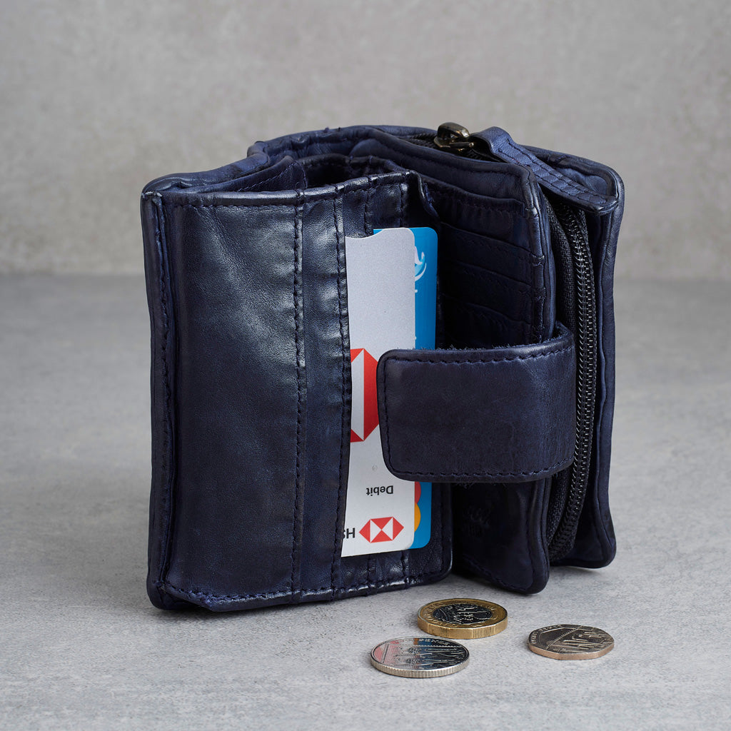 A navy blue leather bifold wallet shown open, with card slots, a zip compartment, and a card partially inserted. Three coins rest in front on a light gray surface against a textured gray background.