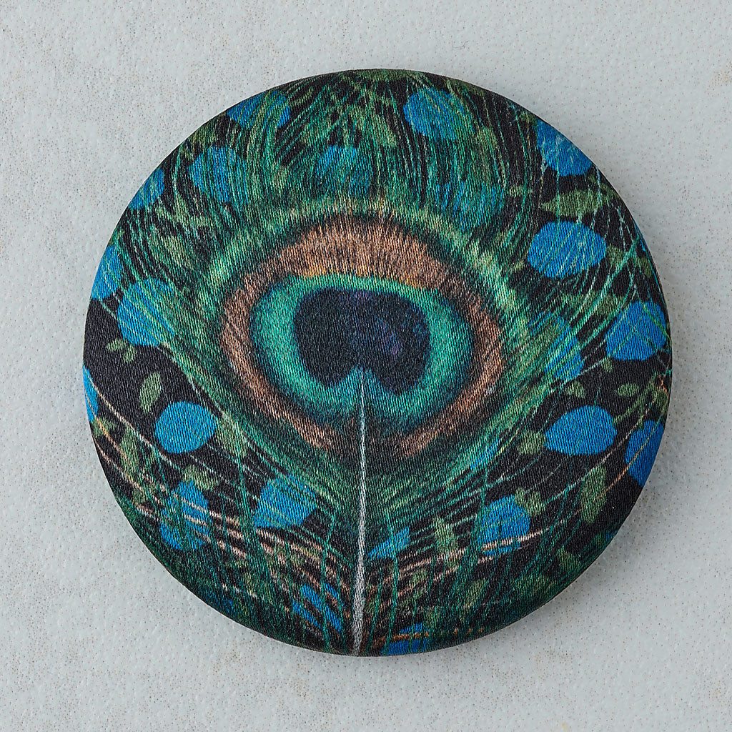 A round pinback button featuring a detailed peacock feather pattern with vibrant teal, blue, green, and brown hues on a dark background, set against a light gray textured backdrop.