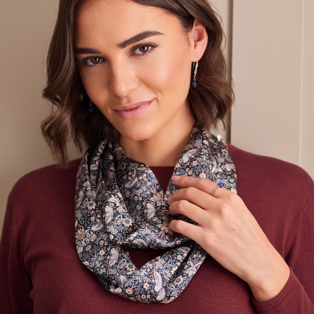 A woman wearing a navy blue paisley and floral patterned infinity scarf with white and beige details, styled over a burgundy long-sleeve top.