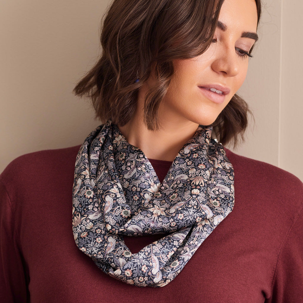 A woman wearing a dark paisley-patterned infinity scarf over a burgundy top, photographed against a plain beige wall.